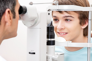 Doctor viewing teen boy's eye through microscope